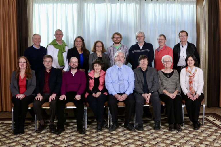 A group photo of 16 people in two rows, half sitting, half standing.